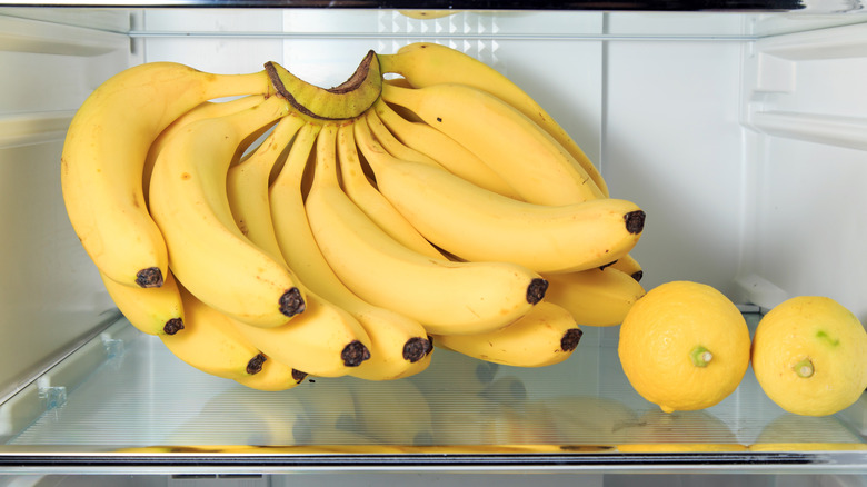 A bunch of bananas next to lemons in a fridge