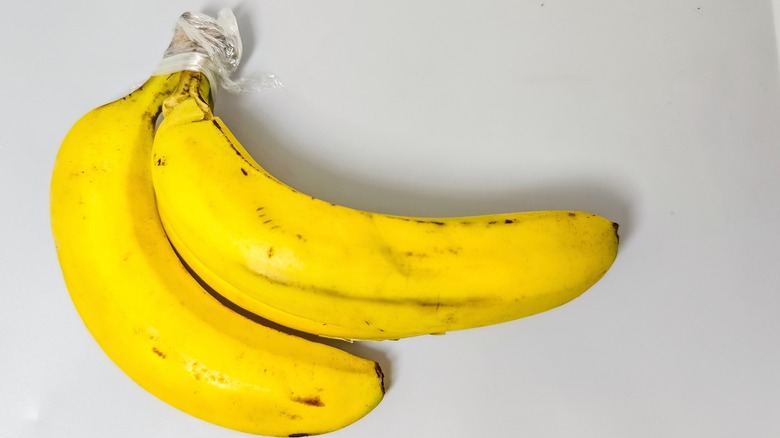 Two bananas covered at the stem with plastic wrap