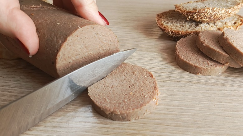 hands cut liverwurst on a wooden board