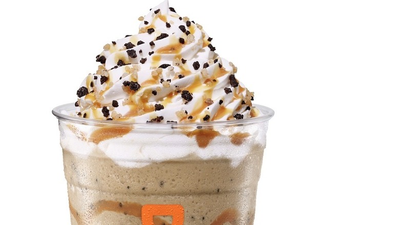 Plastic Dunkin' cup with frozen coffee topped with whipped cream, caramel, and cookie pieces