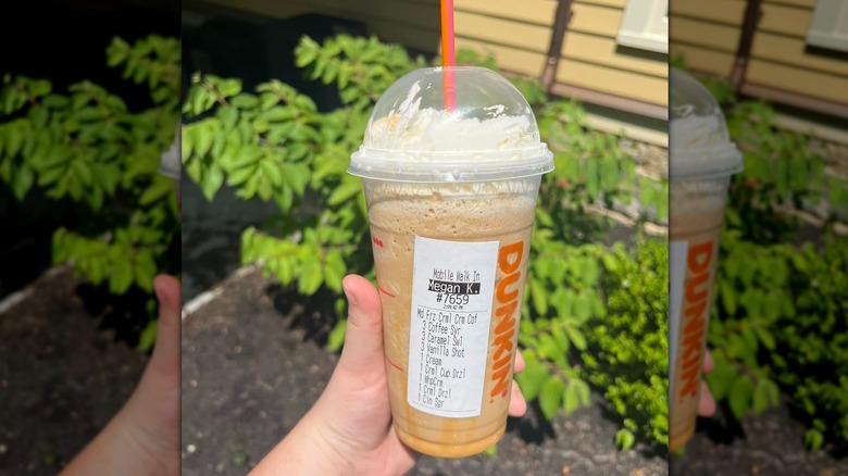 Hand holding plastic cup with Dunkin' frozen coffee