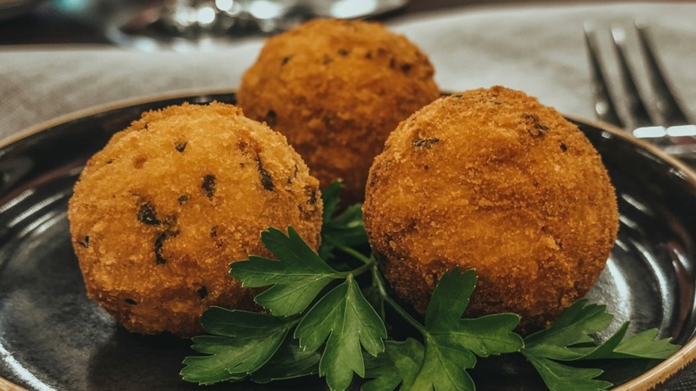 Three codfish cakes on a dark plate