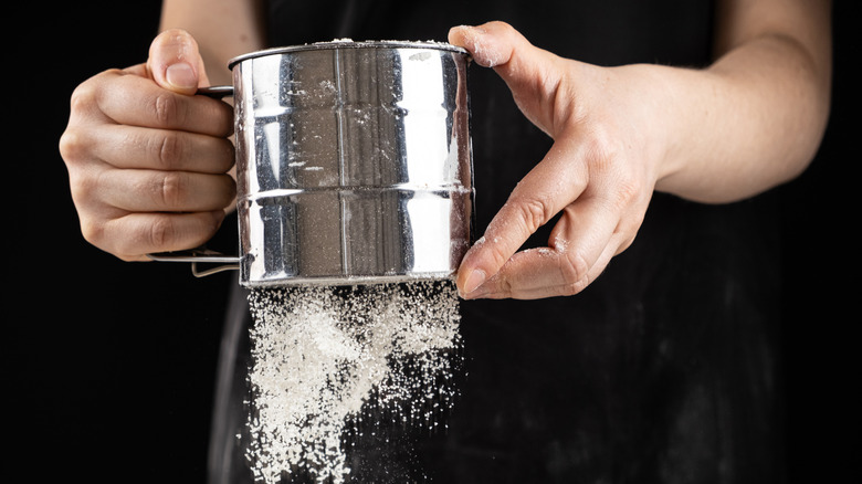 Person sifting flour with stainless steel flour sifter, closeup.