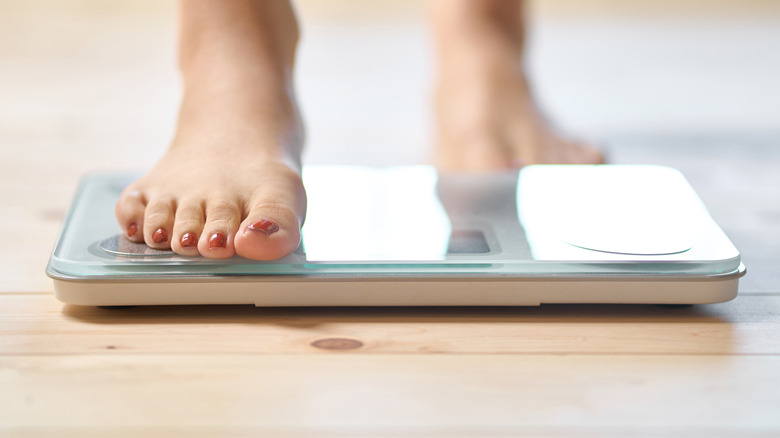 A woman puts one foot on a weigh scale