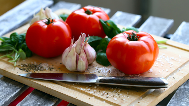 whole tomatoes on cutting board with garlic and basil