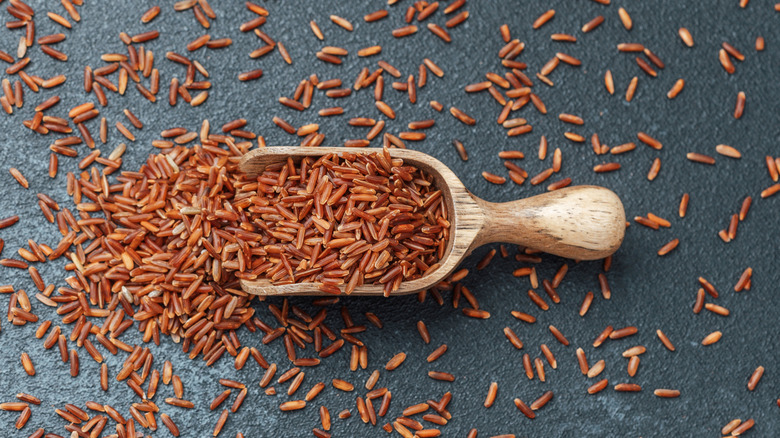 Wooden scoop of red rice spilling on black background