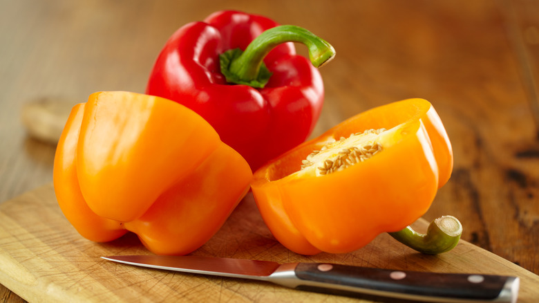 A red bell pepper behind an orange one cut in half