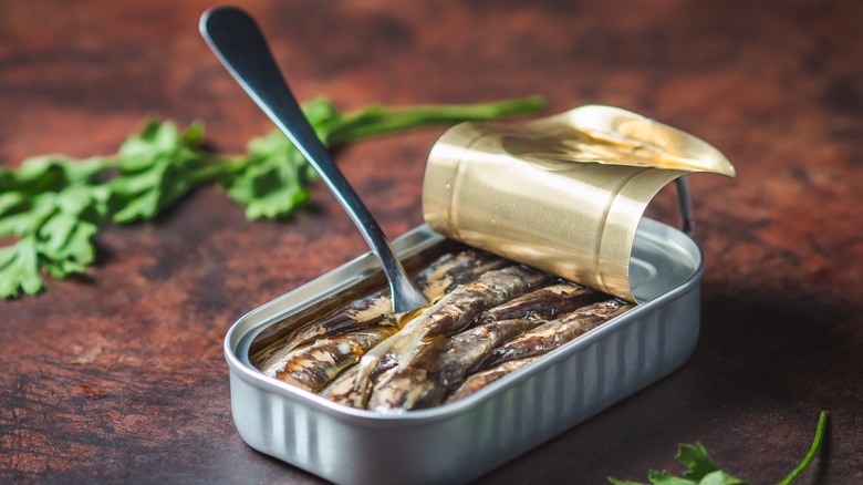 A fork in a can of sardines on a dark wooden table