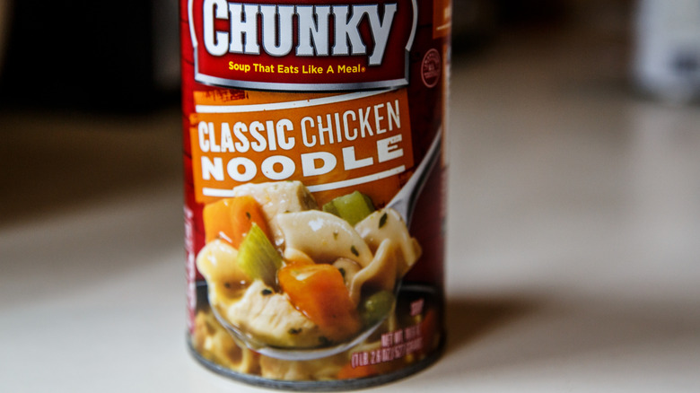 Campbell's Chunky Classic Chicken Noodle Soup prepared and ready to heat and serve for lunch or dinner meals. Red classic label shows soup in can with carrots and celery. Sitting on a kitchen counter.