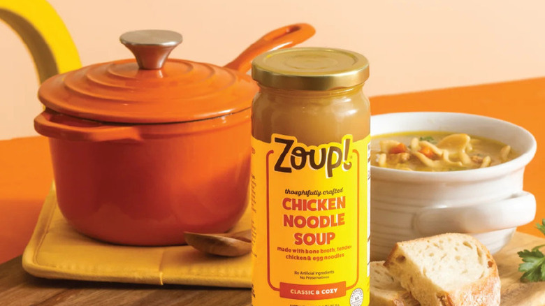 Glass jar of Zoup! Chicken Noodle Soup with soup pot and bowl of soup in background