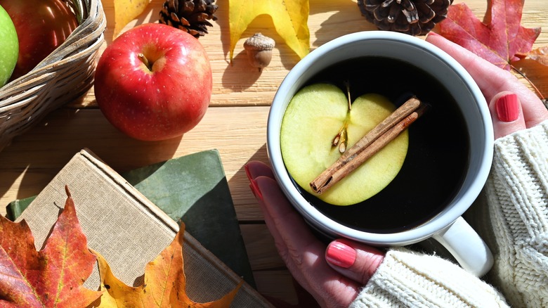 Hands holding a mug of hot apple cider with fall autumn leaves