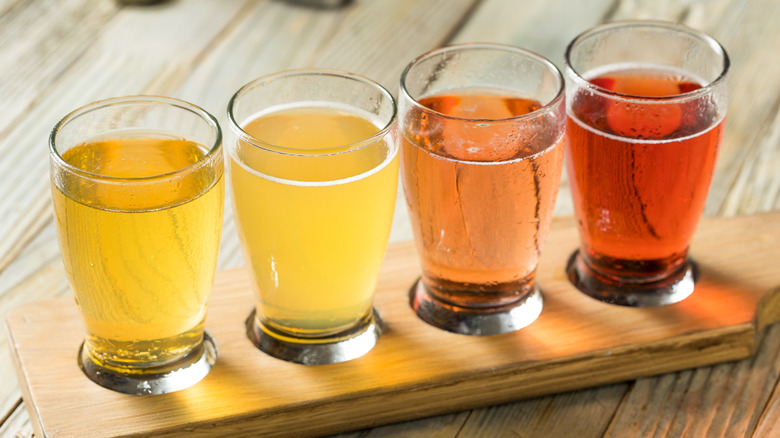 Four glasses of different colored hard ciders on a wooden stand