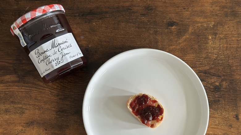 Jar of Bonne Maman Cherry Jam beside white plate with baguette slice