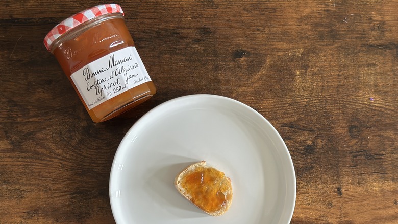 Jar of Bonne Maman Apricot Jam beside white plate with baguette slice