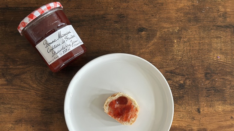 Jar of Bonne Maman Strawberry Jam beside white plate with baguette slice