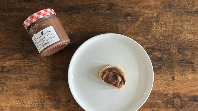 Jar of Bonne Maman Hazelnut and Cocoa Spread beside white plate with baguette slice