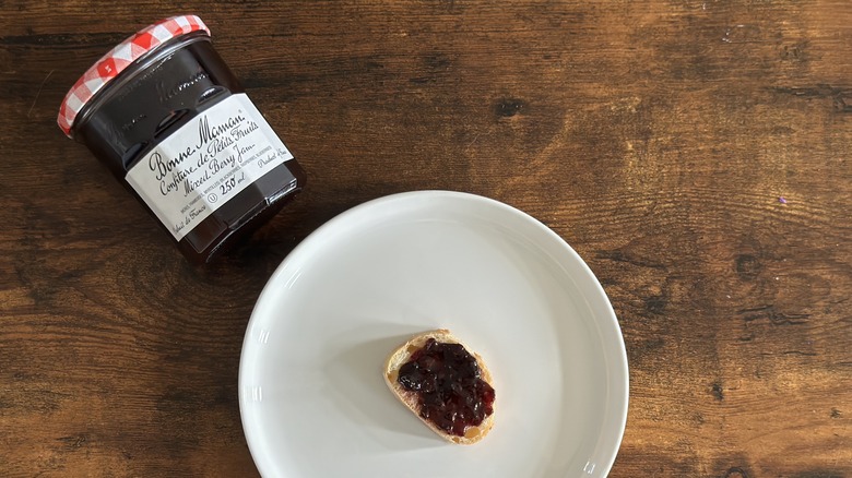 Jar of Bonne Maman Mixed Berry Jam beside white plate with baguette slice