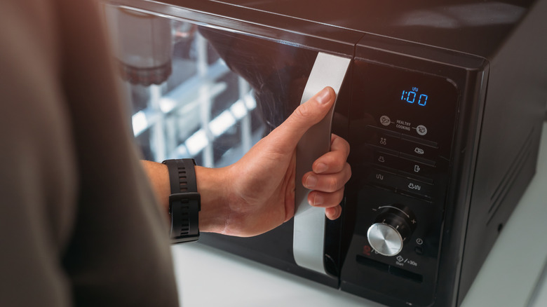 Close up of a man holding the handle on a microwave