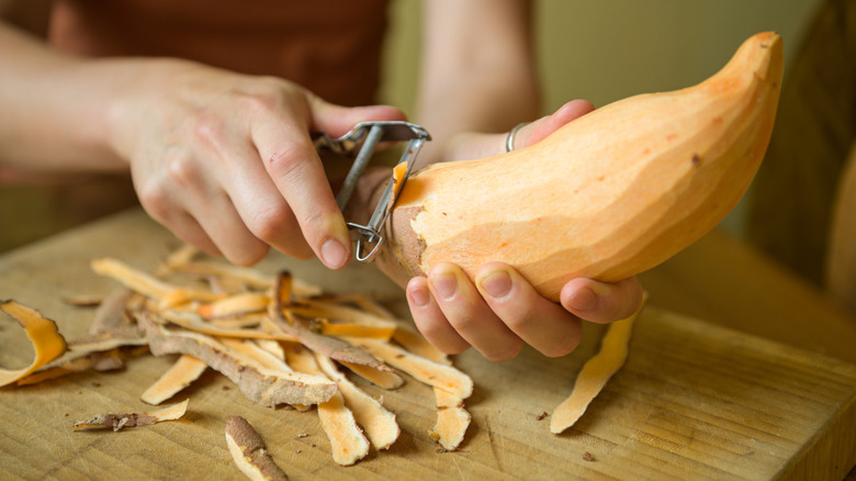 Close-up of hand peeling a sweet potato over a wooden cutting board