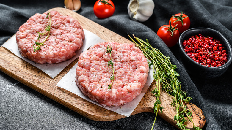 raw burgers on wooden platter