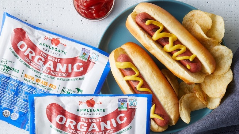 Two hot dogs with mustard and two packages of Applegate Organics hot dogs