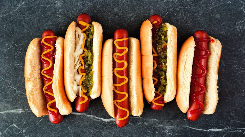 Five hot dogs in buns with classic toppings lined up on counter