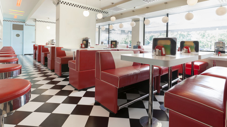 Interior of an American diner, with black and white floor tiles and red booths