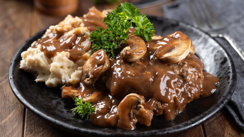 Salisbury steak with mushroom gravy garnished with parsley and mashed potatoes on a black plate