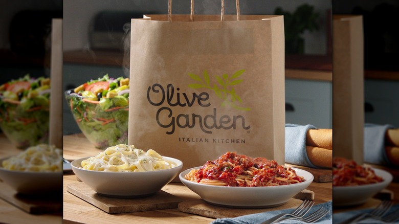 Two plates of Olive Garden food in front of atake-out bag