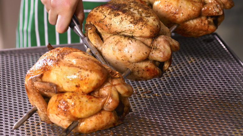 close up of three chickens being taken off a rotisserie spike
