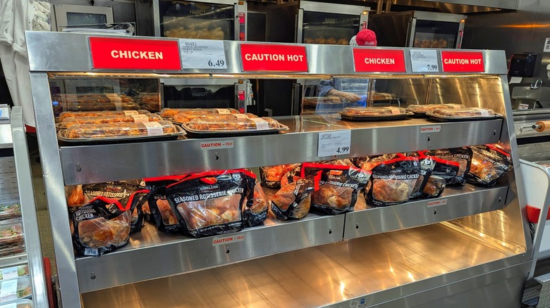 a silver metal display featuring several rotisserie chickens in bags and other meats