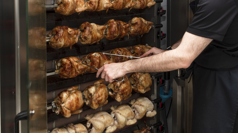 Close-up of a cook turning rotisserie chickens with tongs