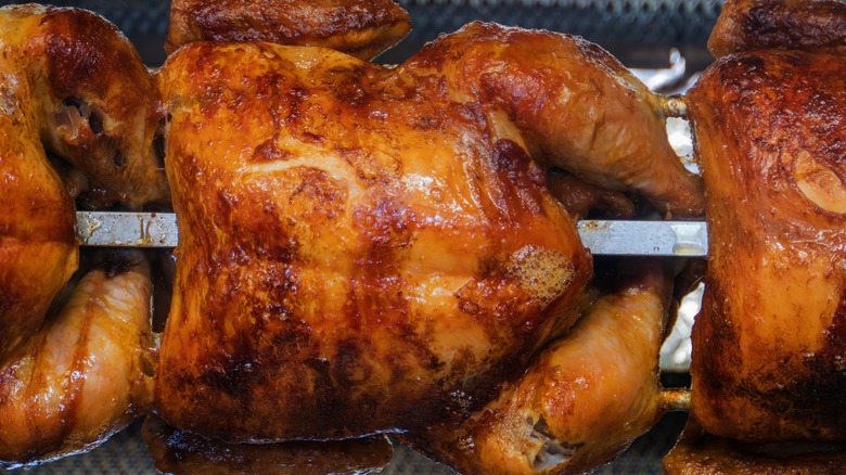 a close-up of a golden brown rotisserie chicken spit-roasted in an oven