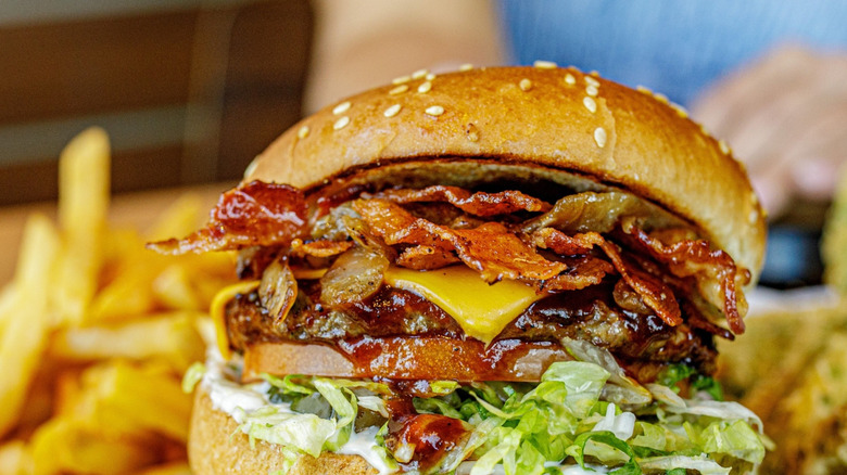 Burger with bacon, cheese, lettuce, and sauce on a sesame seed bun