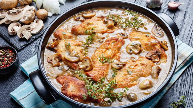 Chicken Marsala, Italian-American dish of golden pan-fried chicken cutlets and mushrooms in a rich Marsala wine sauce in a black ceramic dish on a wooden table, view from above, close-up