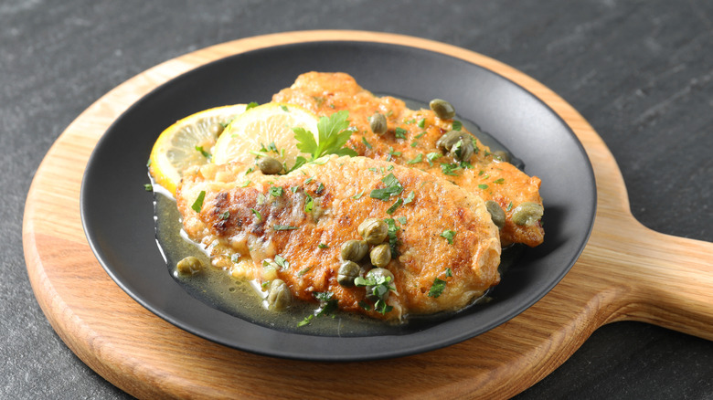 Delicious chicken piccata with herbs and lemons on black table