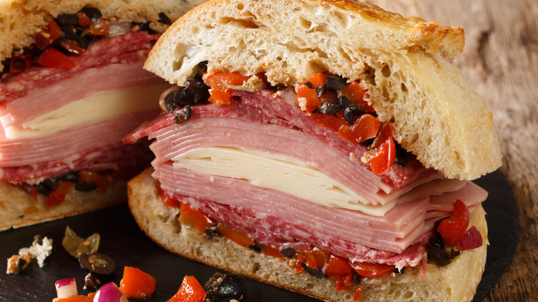 Muffuletta sandwich filled with olive salad, cheese, salami and ham close-up on a slate board on the table