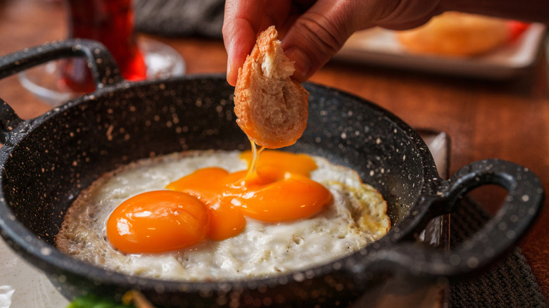 A hand dipping bread into sunny side up eggs