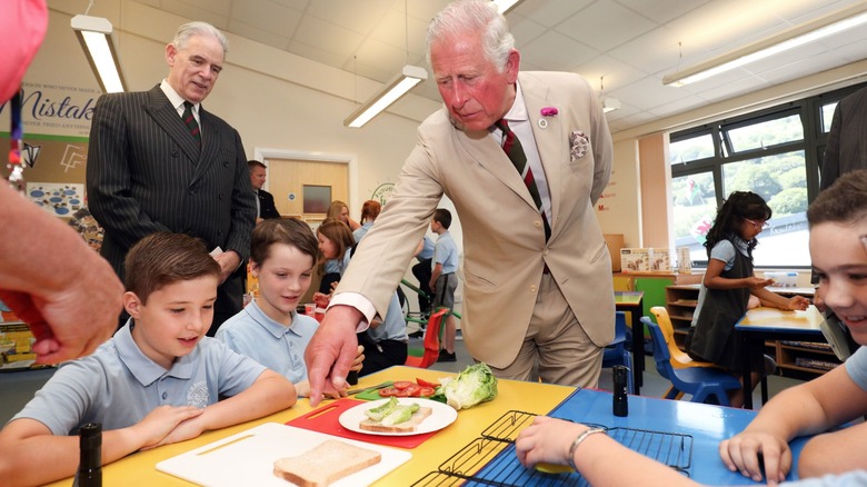 Prince Charles in a school pointing at an unmade sandwich