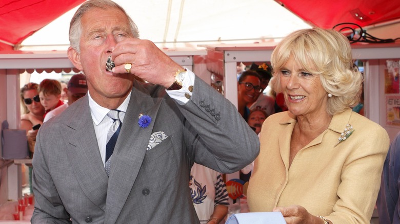 King Charles eating an oyster and Queen Camilla holding out a napkin
