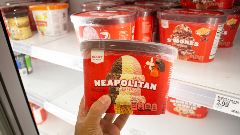 A hand holding a carton of Market Pantry Neapolitan ice cream, on display at a Target store
