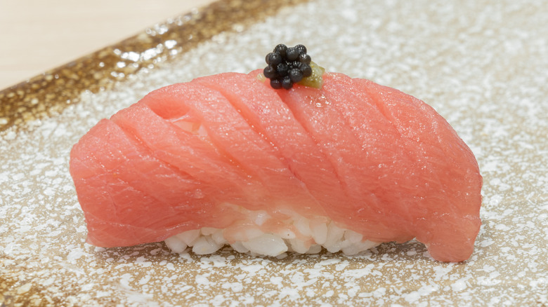 Maguro nigiri sushi topped with black caviar, served on gold speckled plate