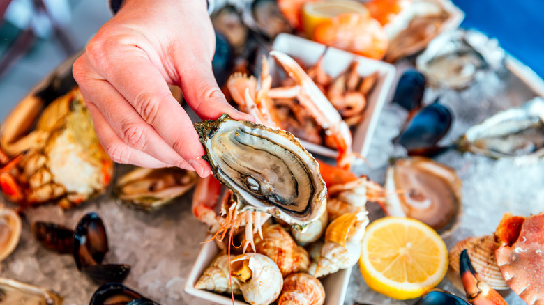 holding an oyster above a lot of seafood