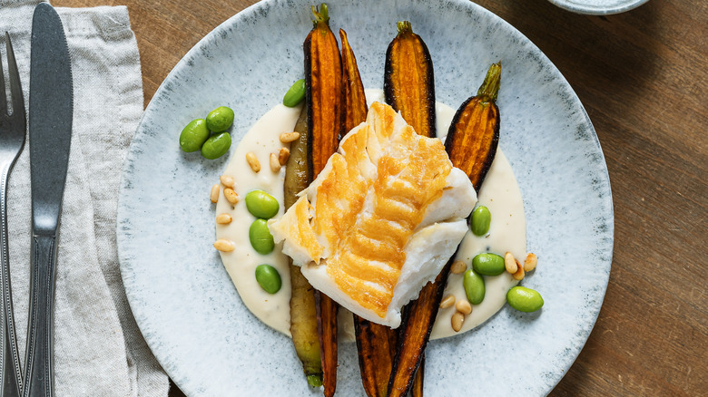 A plate of cod fillet on a bed of vegetables