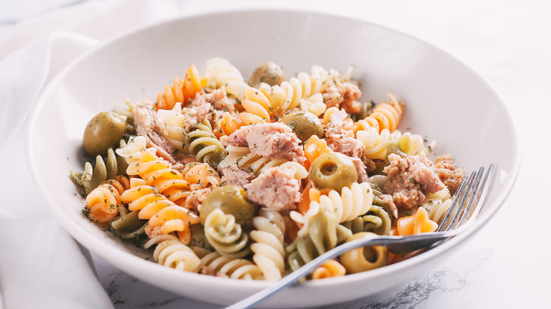 Bowl of pasta with tuna and olives on marble surface