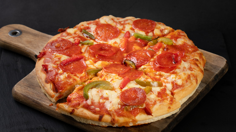 Pan pizza on wooden paddle with pepperoni, green peppers, and cheese