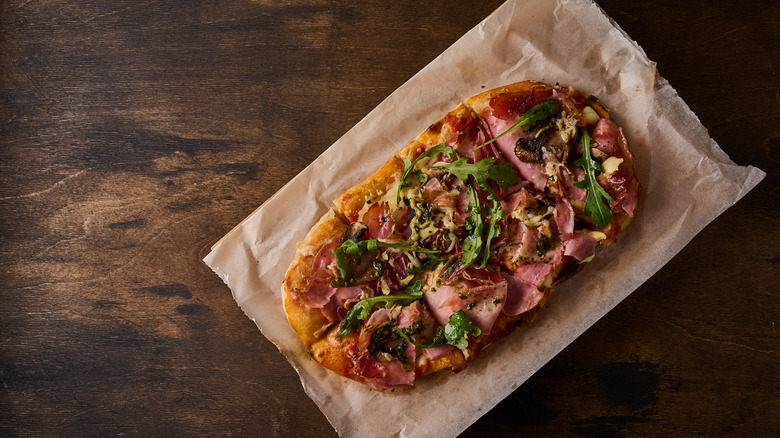 Rectangular Roman pizza with prosciutto, tomatoes, mozzarella, mushrooms, and arugula