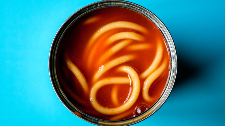 An open can of spaghetti in tomato sauce on a blue background