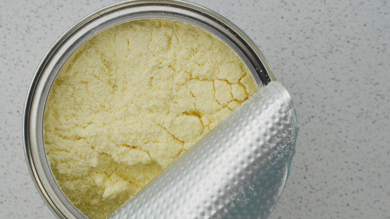 Top-down close-up of an opened can of baby formula on a speckled gray surface