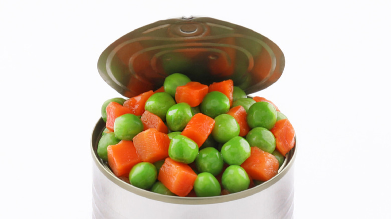 A close up of an open can of peas and carrots on a white background